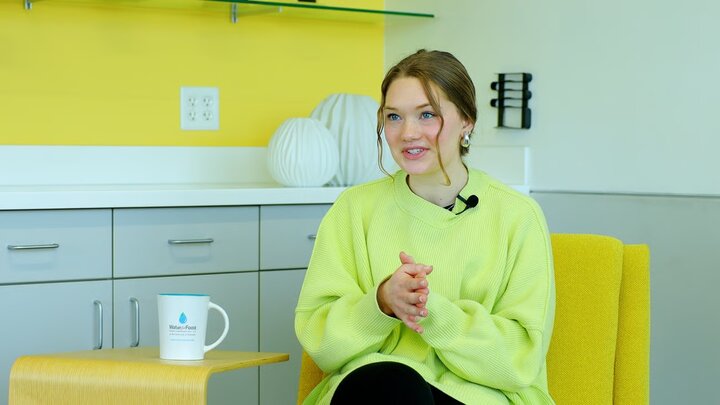 Woman in a lime green sweater sitting on a yellow chair, with a mug and decor in a bright room.